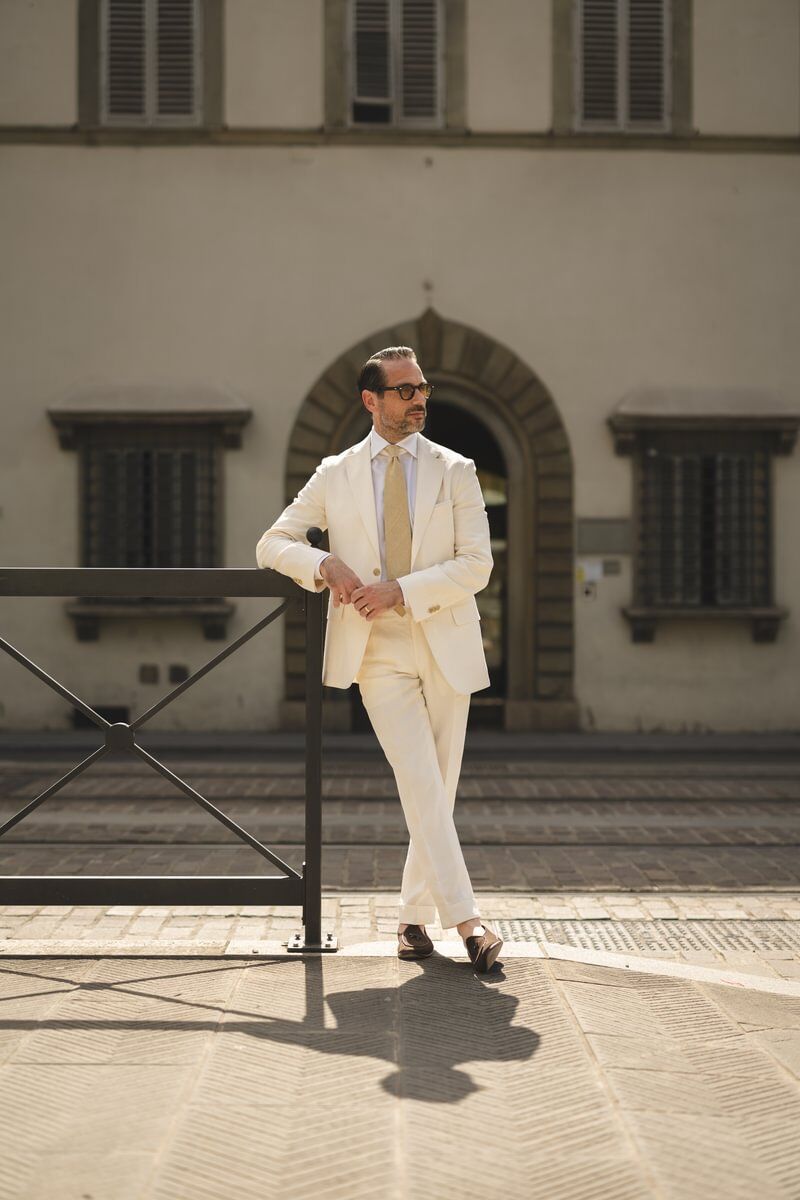 Brian wearing a cream linen suit with a white shirt and beige tie, styled with sunglasses and loafers