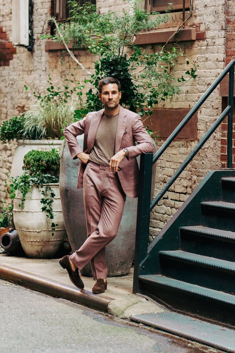 Shane wearing a dusty rose blend suit paired with a taupe crewneck tee and loafers, styled casually by Michael Andrews Bespoke in a garden alley setting
